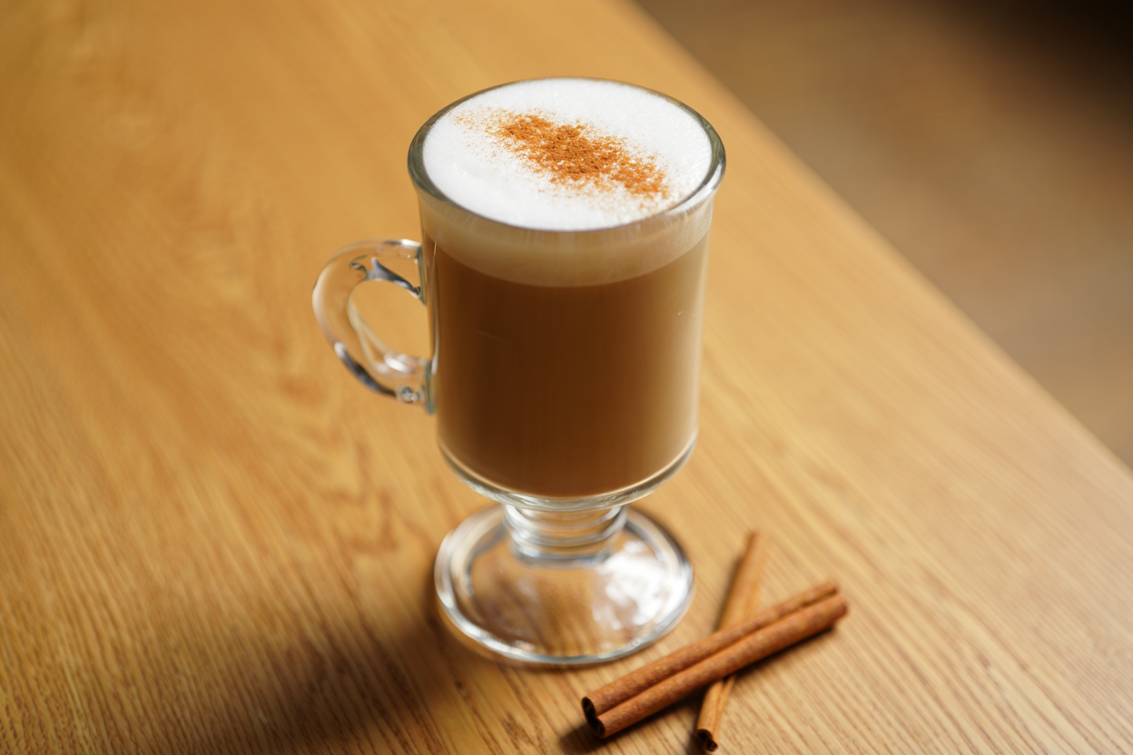 Creamy chai tea latte in a tall glass with milk froth and a dusting of cinnamon on a light oak surface